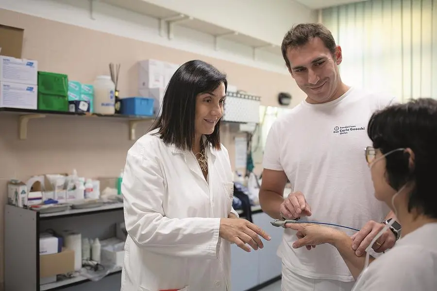 Elvia Battaglia, affiancata da Massimo Garegnani, tecnico di Neurofisiopatologia alla Fondazione Don Gnocchi, spiega a una paziente come posizionare il sensore del saturimetro prima di una polisonnografia. La foto è di Costanza Longhini.